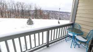 A covered outdoor area with a snow-covered deck, a small Christmas tree, and two blue metal chairs. - Seven Springs Stoneridge 3 Bedroom Standard Condo, Mountain Views! by RedAwning (Champion)