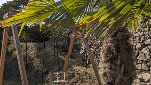 A wooden swing set with a stone wall in the background. - Le Cottage ****, 4-bedroom house in the heart of the historic center of Kaysersberg, with parking facilities. (Kaysersberg-Vignoble)