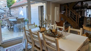 A dining area with a table set for four, surrounded by white chairs, a patterned rug, and a view of the outdoor patio. - Le Cottage ****, 4-bedroom house in the heart of the historic center of Kaysersberg, with parking facilities. (Kaysersberg-Vignoble)