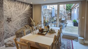 A dining area with a table set for six, surrounded by chairs, with a patterned rug on the floor and a decorative wall to the left. - Le Cottage ****, 4-bedroom house in the heart of the historic center of Kaysersberg, with parking facilities. (Kaysersberg-Vignoble)
