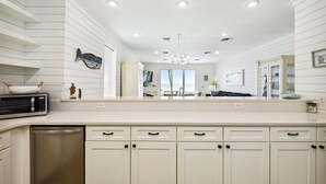 A modern kitchen with white cabinetry, a large island, and a view to the living area.