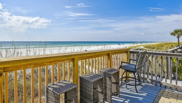 A wooden deck with wicker furniture overlooking a beach.