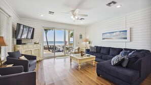 A living room with a TV, two sofas, a coffee table, and a view of the beach through a sliding door.