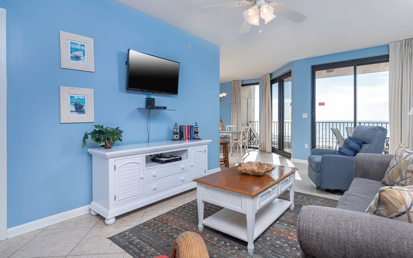 A living room with a flat-screen TV, white entertainment unit, and a balcony with a view.