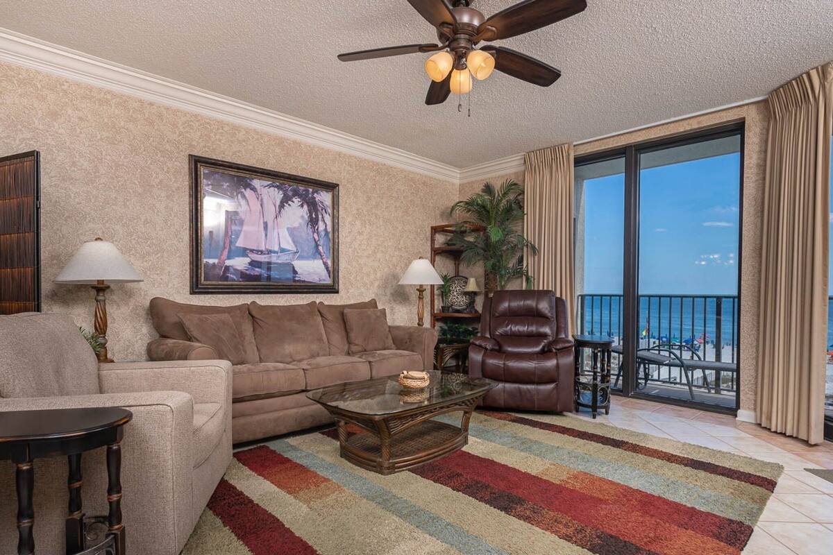 Ein Wohnzimmer mit Sofa, Sesseln, Couchtisch und Blick auf den Ozean durch eine große Schiebetür.