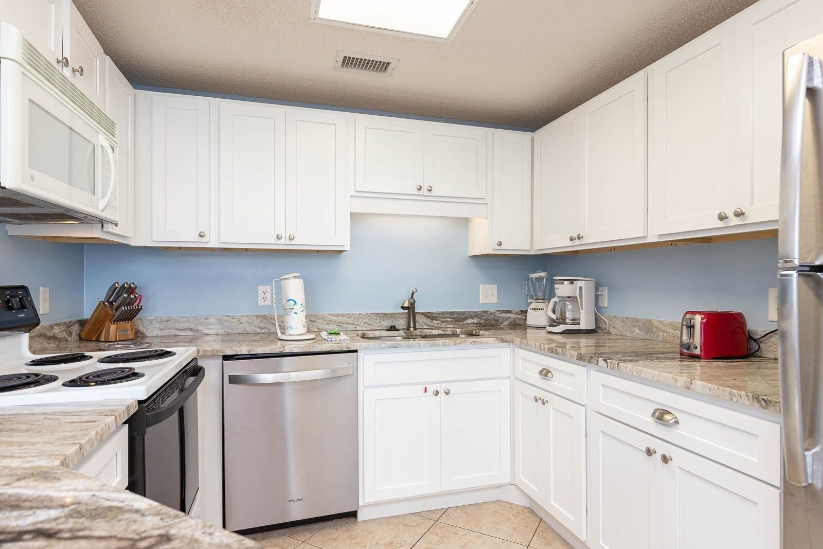 A modern kitchen with white cabinets, a stainless steel stove, a dishwasher, a red toaster, and a coffee maker.