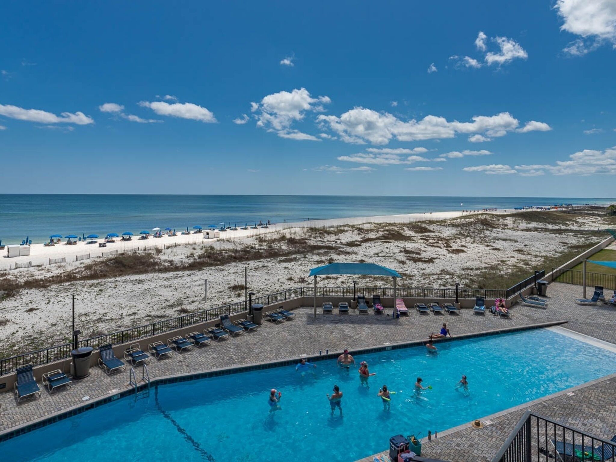 Ein Schwimmbecken mit Personen, ein Strand und ein klarer Himmel.