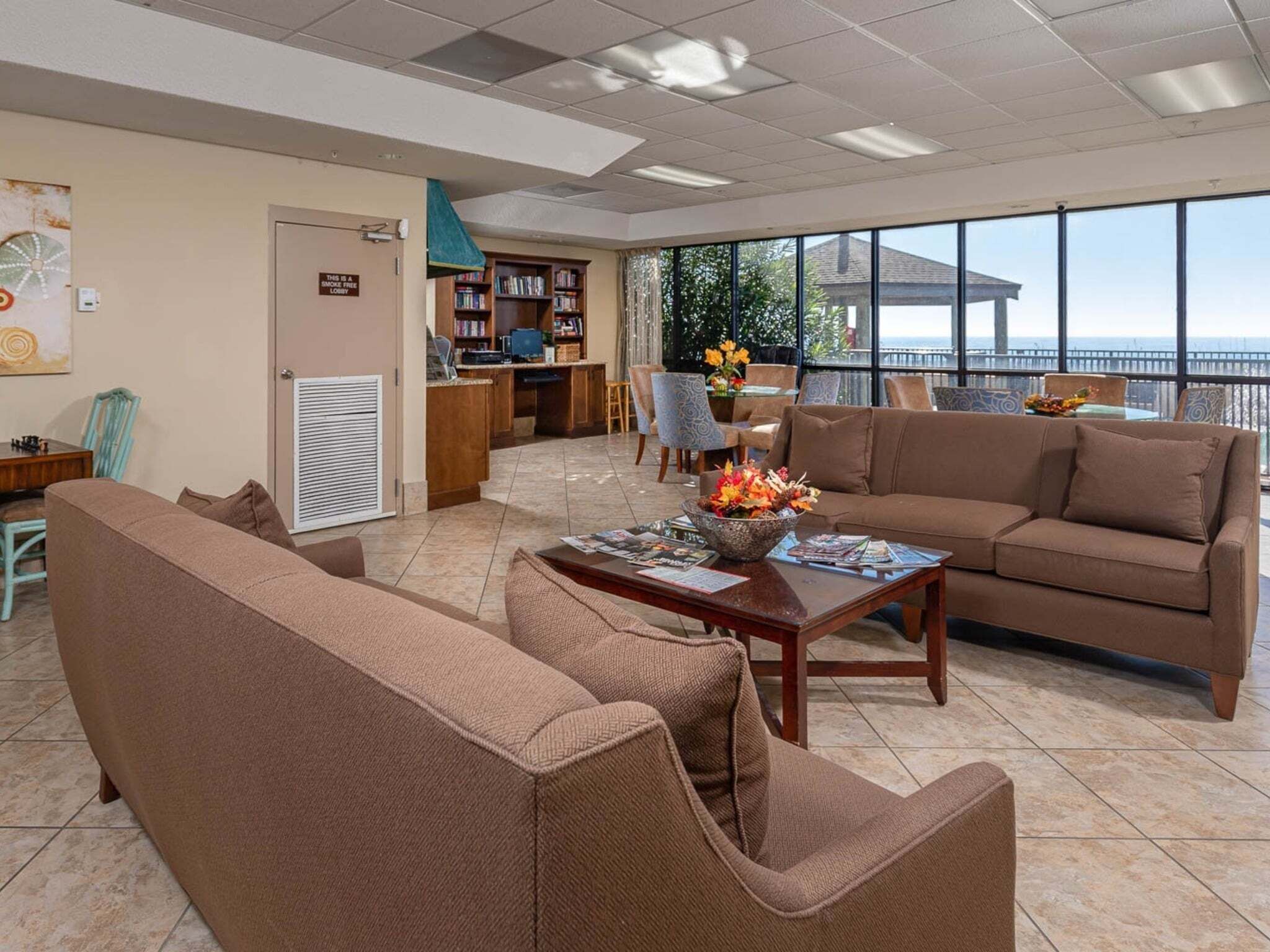A spacious lounge area with a sofa, armchairs, a coffee table, and a desk with a computer. There is a bookshelf and a sign indicating a smoke-free lobby.