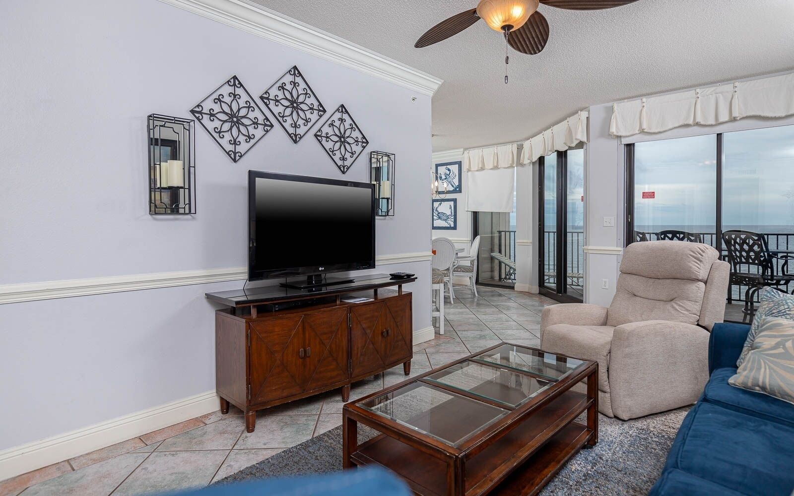 A living room with a flat-screen TV, a glass coffee table, a beige armchair, and a blue sofa.