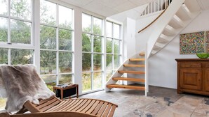 Un interno moderno con una sedia in legno, una scala e ampie finestre.