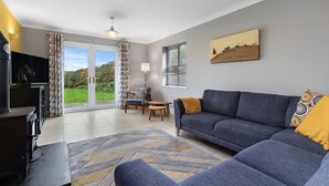 A modern living room with a grey sofa, a fireplace, and a large window offering a view of the outdoors. - A Family Home Near Estuary & Llansteffan Castle (Llansteffan)