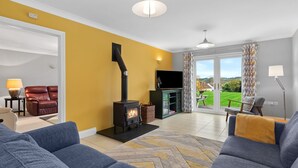 A living room with a fireplace, sofas, a TV, and a view through a glass door. - A Family Home Near Estuary & Llansteffan Castle (Llansteffan)