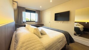 A hotel room with a large bed, a TV mounted on the wall, and a window with curtains. - Pousadinha Campos (Campos do Jordão)