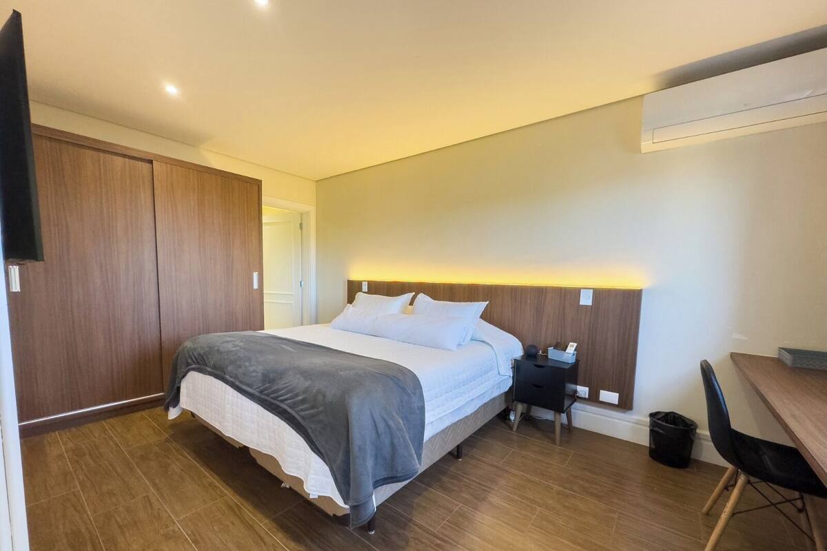Een moderne hotelkamer met een groot bed, een houten garderobe, een nachtkastje en een klein bureau.