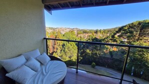 A balcony with a round bed and a view of a hilly landscape. - Pousadinha Campos (Campos do Jordão)