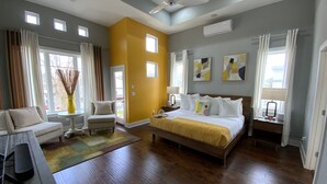 A modern bedroom with a large bed, a sofa, a chair, and a small table. There are windows with curtains, a ceiling fan, and artwork on the walls. -  Stay in Style Where the Musicians Live 6-beds, 4-bedroom, 3-bath   (Nashville)