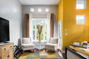 A room with a TV, two chairs, a small table, and a window with curtains.