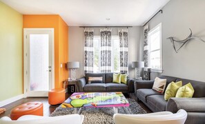 A living room with a sofa, ottoman, and coffee table, a door, and patterned curtains.