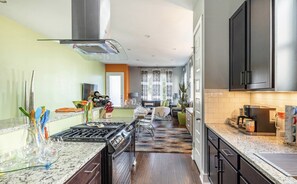 A modern kitchen with a gas stove, stainless steel appliances, and a dining area with a sofa and coffee table.