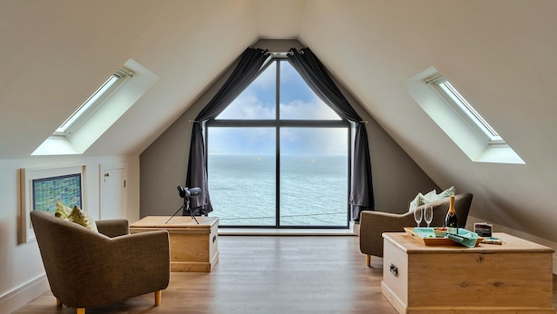 Quarto estilo loft moderno com um grande domo, vista para o mar e um espaço de estar aconchegante com um baú de madeira e uma luminária.