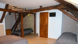 Une chambre située dans un espace de type « loft », avec une échelle en bois, une porte en bois et deux lits.