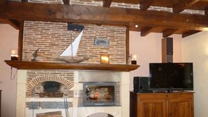 Un salon rustique avec une cheminée en briques, un téléviseur posé sur un meuble en bois et un manteau de cheminée en pierre.