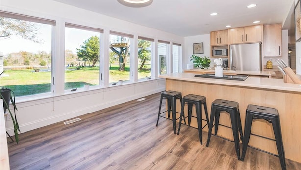 Une cuisine moderne dotée de grandes fenêtres, d’un plancher en bois et d’un coin bar avec des tabourets.