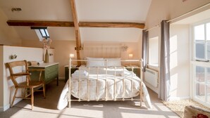 A bedroom with a wooden ceiling, a bed with white bedding, a desk with a chair, and a window with curtains.