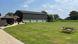 A large barn with a gravel driveway and a picnic table in a grassy field.
