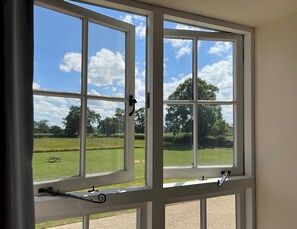 Enjoy a serene view of the lush green field and tree-lined horizon from the large window.