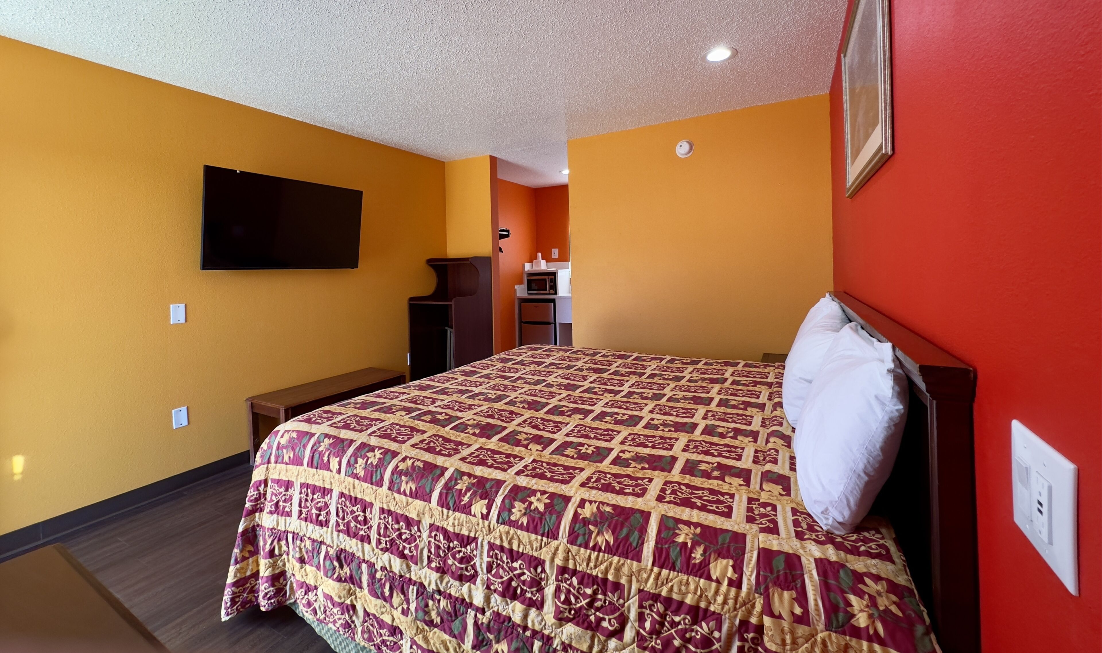 A hotel room with a bed, a television mounted on the wall, a small table, and a microwave.