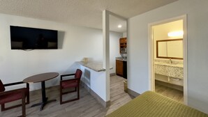 Un espacio habitable compacto con comedor, kitchenette y televisor montado en la pared.
