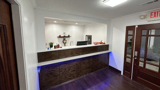 Un área de recepción con un mostrador de madera oscura, una pared blanca y una señal de salida.