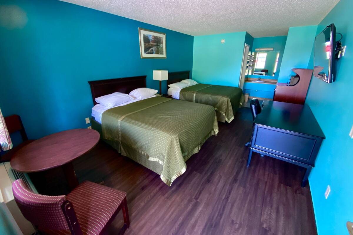 Une chambre d’hôtel avec deux lits, un bureau, une chaise, une commode, un miroir et un tableau au mur.