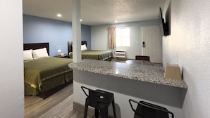 Una habitación de hotel compacta con kitchenette, dos camas, televisión y un pequeño rincón bar.