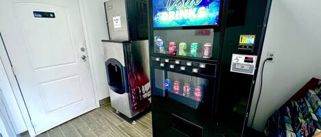 Un distributeur automatique avec une pancarte indiquant « boissons fraîches », un réfrigérateur Red Bull et diverses canettes de boissons.
