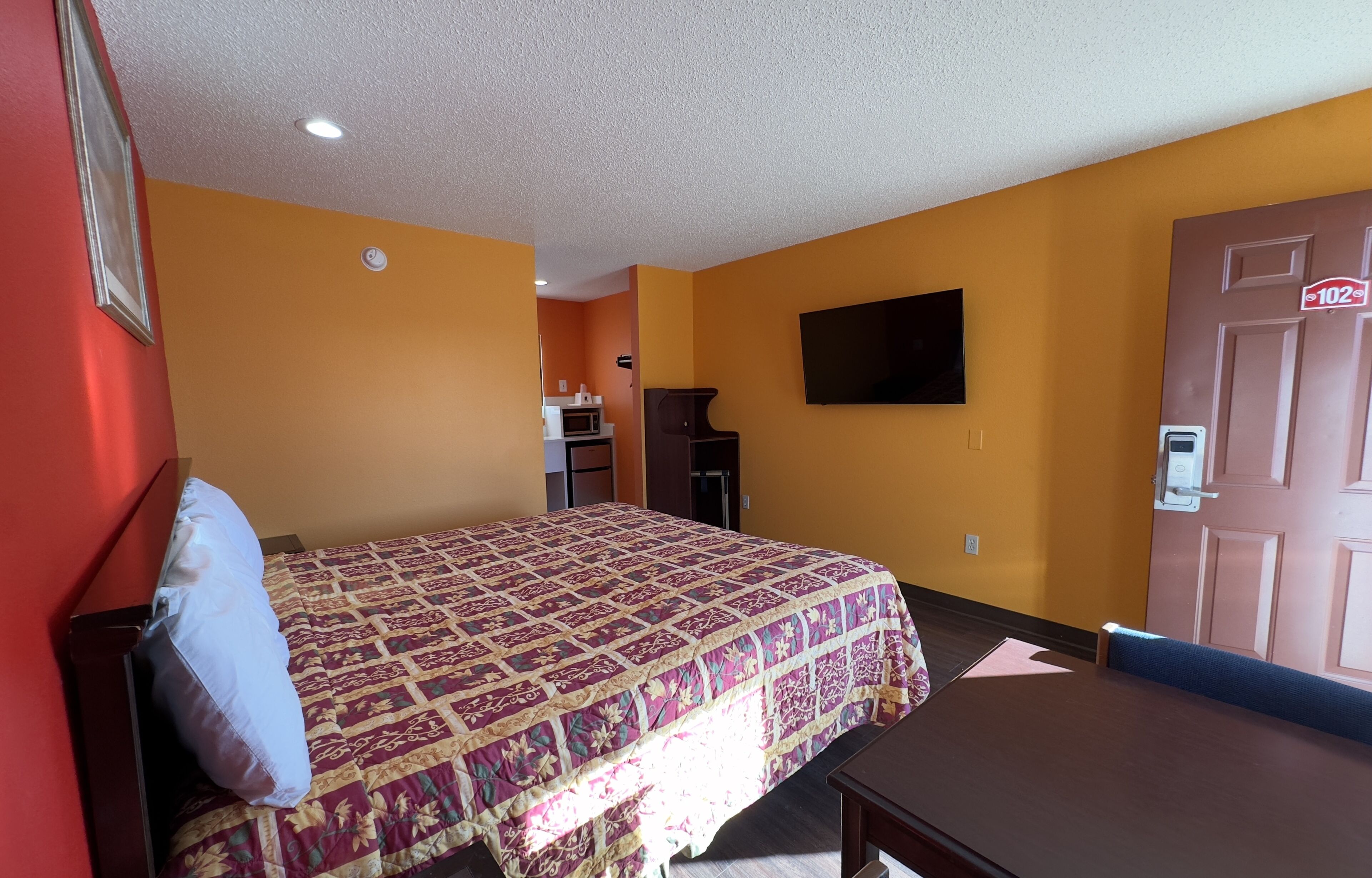 Een hotelkamer met een bed, een bureau, een televisie en een deur met een bordje van een radiozender.
