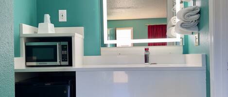 A bathroom with teal walls, a white sink, a mirror, a microwave, and a trash can.