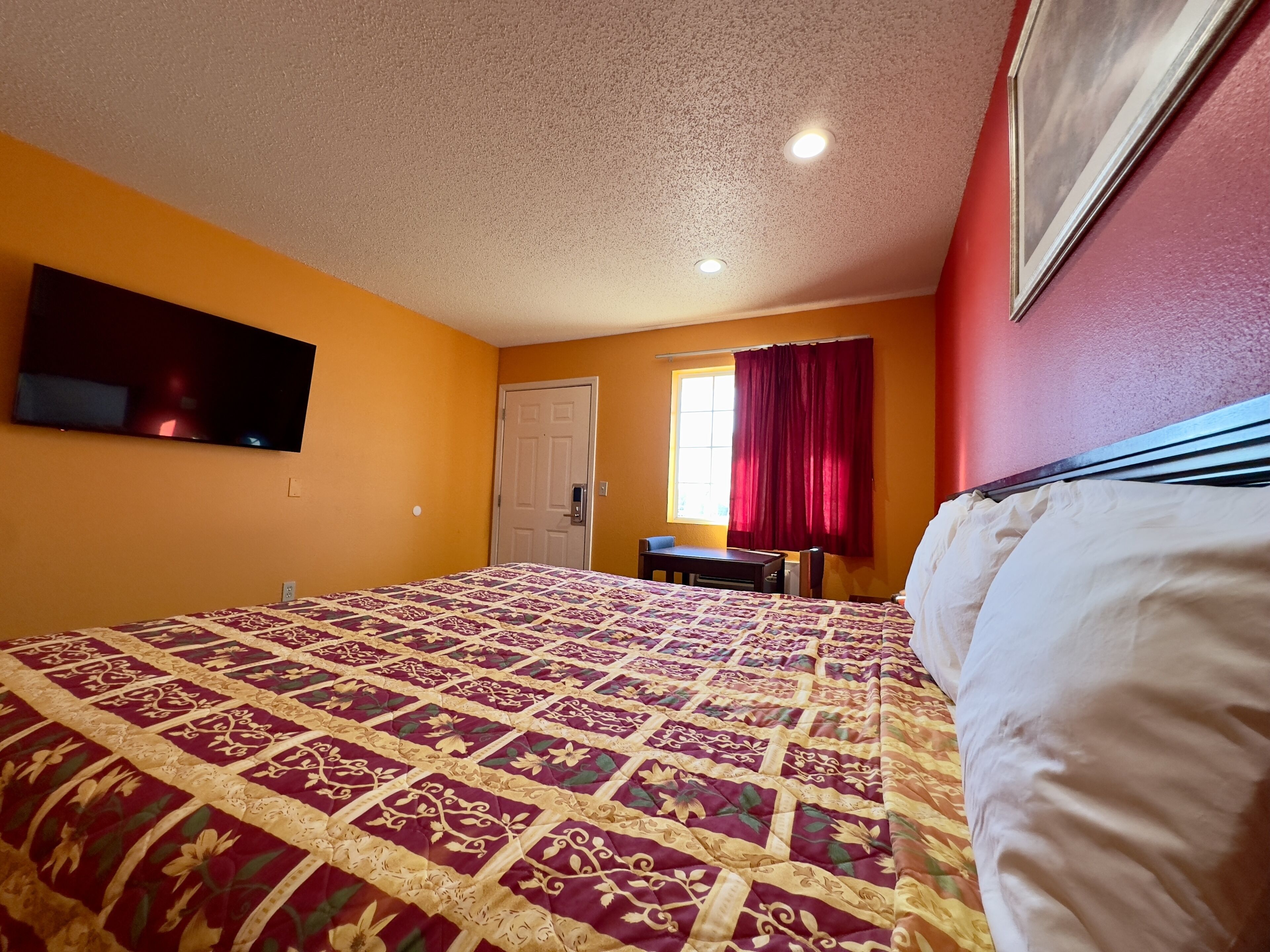 Een hotelkamer met een groot bed, een flatscreen-tv aan de muur, een raam met rode gordijnen en een deur.