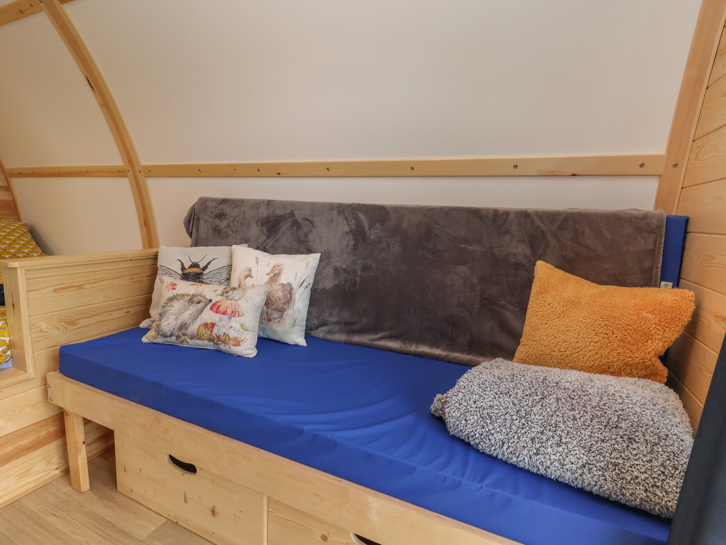 Una habitación acogedora y compacta con cama de madera, colchón azul y cabecera gris.