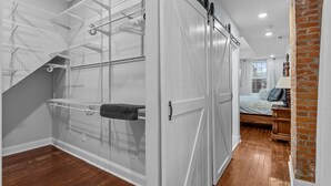 A room with a walk-in closet, a bed with a headboard, and a brick wall.
