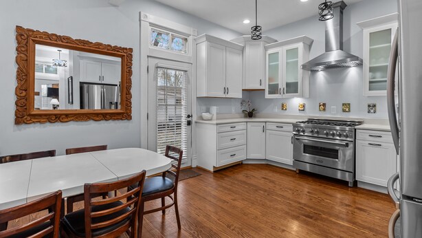 A modern kitchen with white cabinets, a stainless steel stove, and a large wooden dining table.