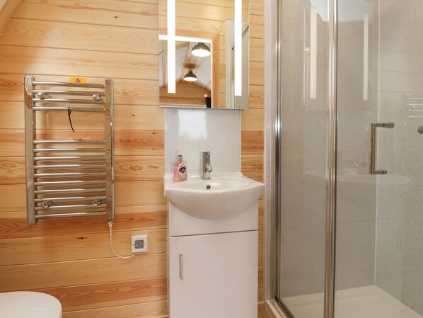 A bathroom with a wooden wall, a white sink, a mirror, and a glass shower enclosure.