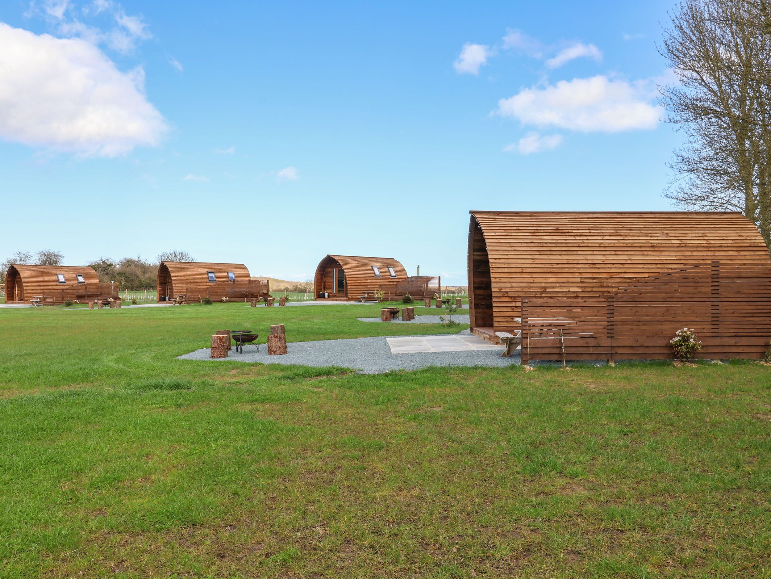 A series of wooden cabins with large arched entrances, set in a grassy field with a clear sky.