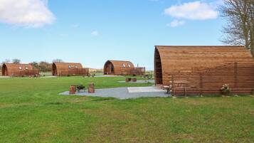 A series of wooden cabins with large arched entrances, set in a grassy field with a clear sky.