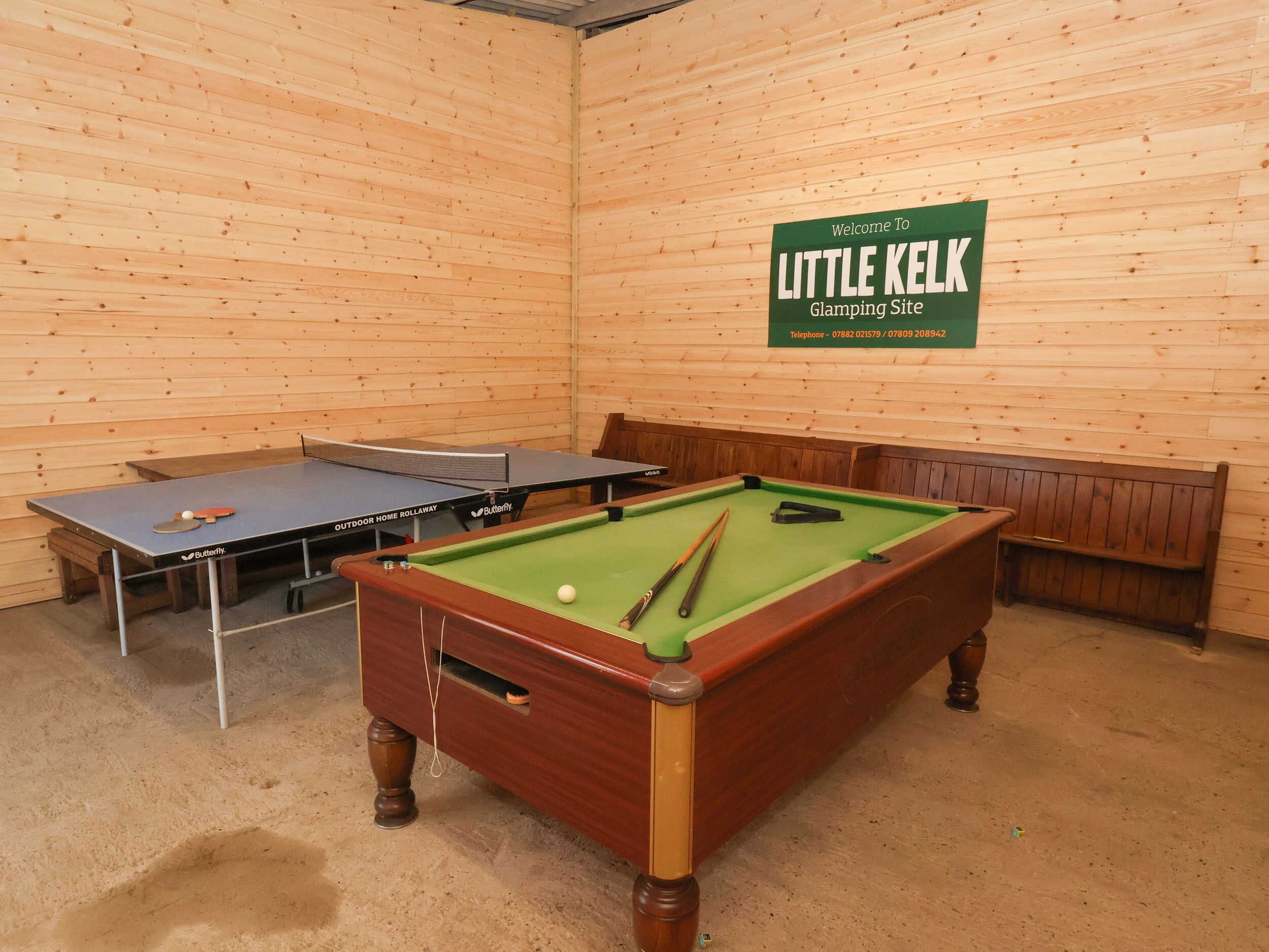 A billiards room with a pool table, two ping pong tables, and a green sign indicating it's the Glamping Site at Little Kelk.