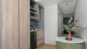 Une cuisine compacte avec des meubles en bois, un four à micro-ondes encastré et un évier. On y trouve un petit coin repas avec une table ronde et une seule chaise.