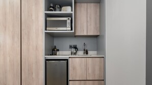 Une cuisine compacte équipée d’un four à micro-ondes encastré, d’un petit réfrigérateur et de meubles de rangement en bois.