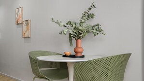 Un coin repas avec une table ronde, deux chaises vertes, un vase orné de feuillage vert et deux œuvres d’art accrochées au mur.