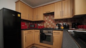 Une cuisine avec des meubles de rangement en bois, un réfrigérateur noir, un four à micro-ondes, une cuisinière et une machine à café.